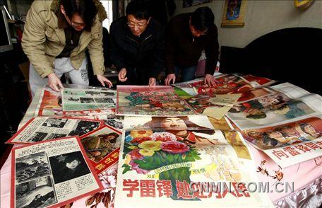 3月1日，房冠龍（中）在家中整理關(guān)于雷鋒的宣傳海報(bào)。
